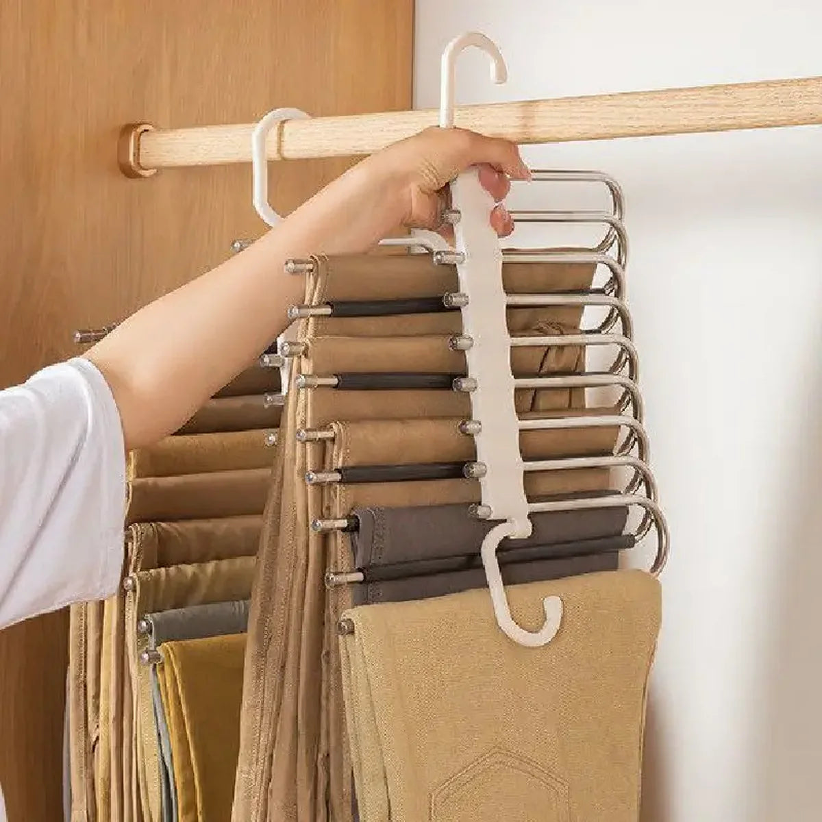 A hand is hanging a beige garment onto a stainless steel multi-layer hanger rack.