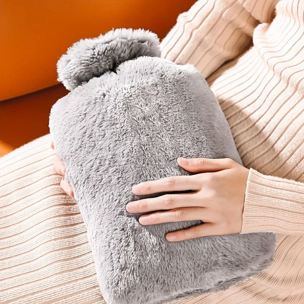 A hand is holding a large gray plush hot water bottle against a beige knitted fabric.