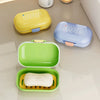 Three colorful leakproof travel soap containers in yellow, blue, and green are displayed on a light surface.