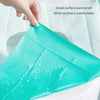 A teal disposable toilet seat cover is shown being placed on a white surface.