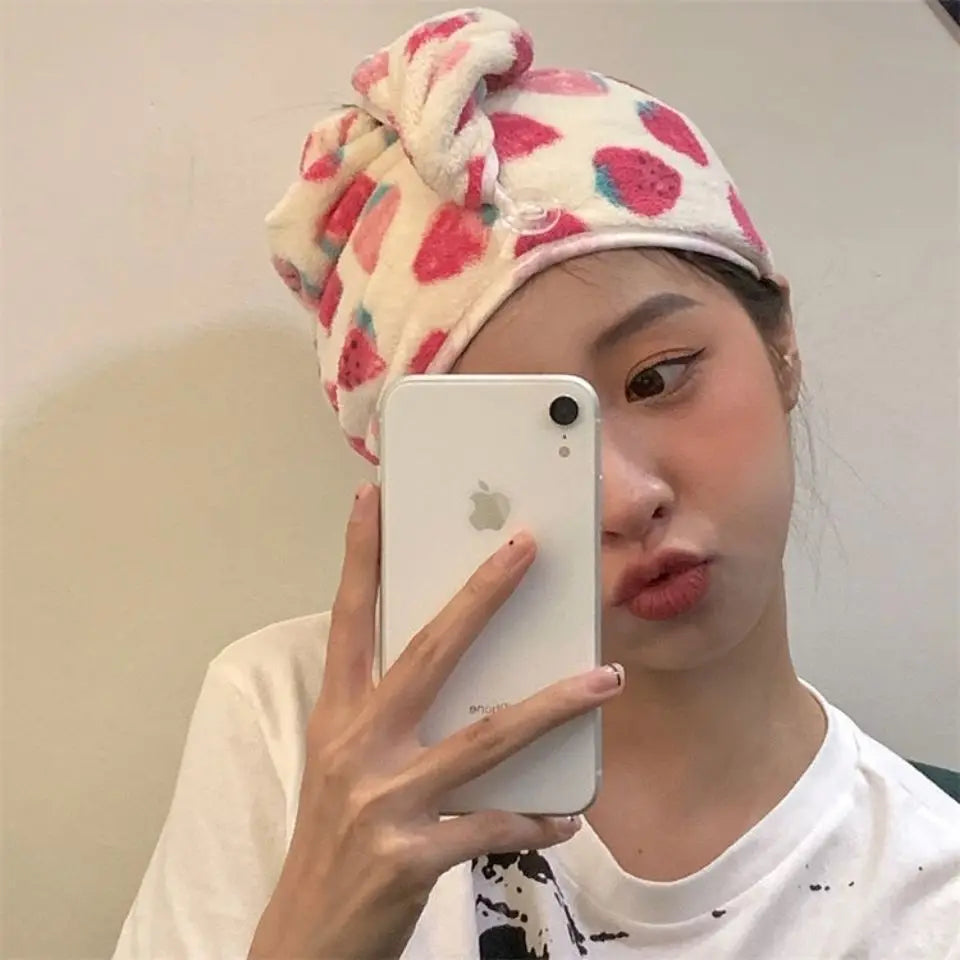 A woman wearing a strawberry print quick-drying hair towel headscarf holds a white smartphone in front of her face.