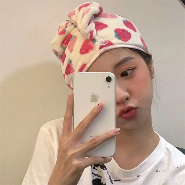 A woman wearing a strawberry print quick-drying hair towel headscarf holds a white smartphone in front of her face.