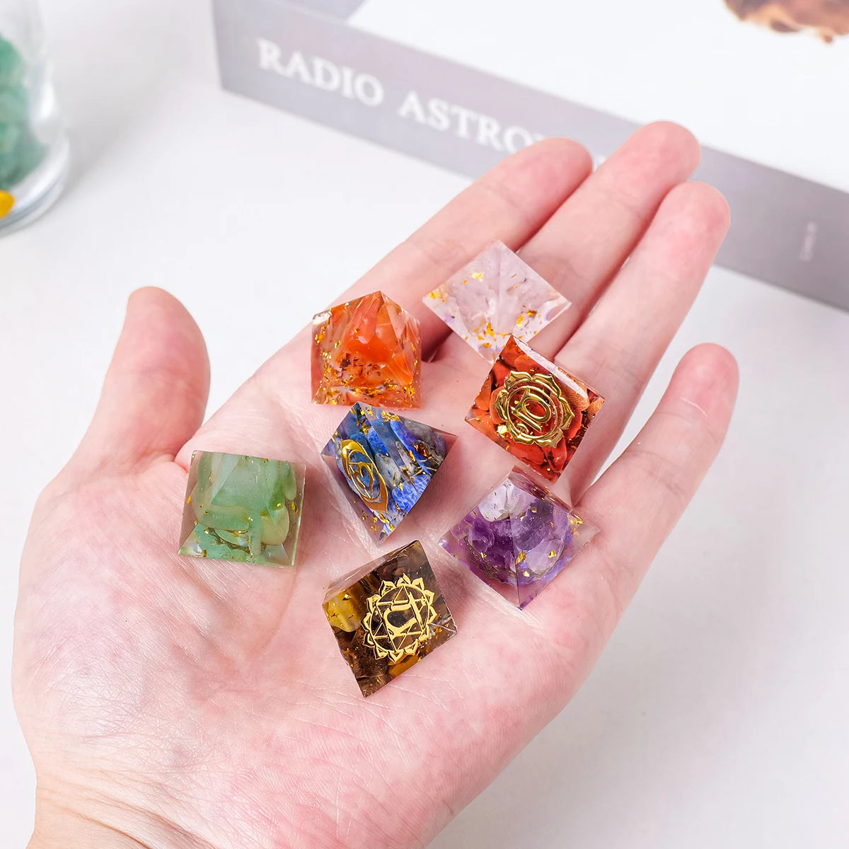 A hand holds a set of natural stone chakra pyramids featuring various colors like orange, pink, green, and purple.