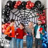 Four people posing in front of a balloon garland featuring blue, red, and black balloons.