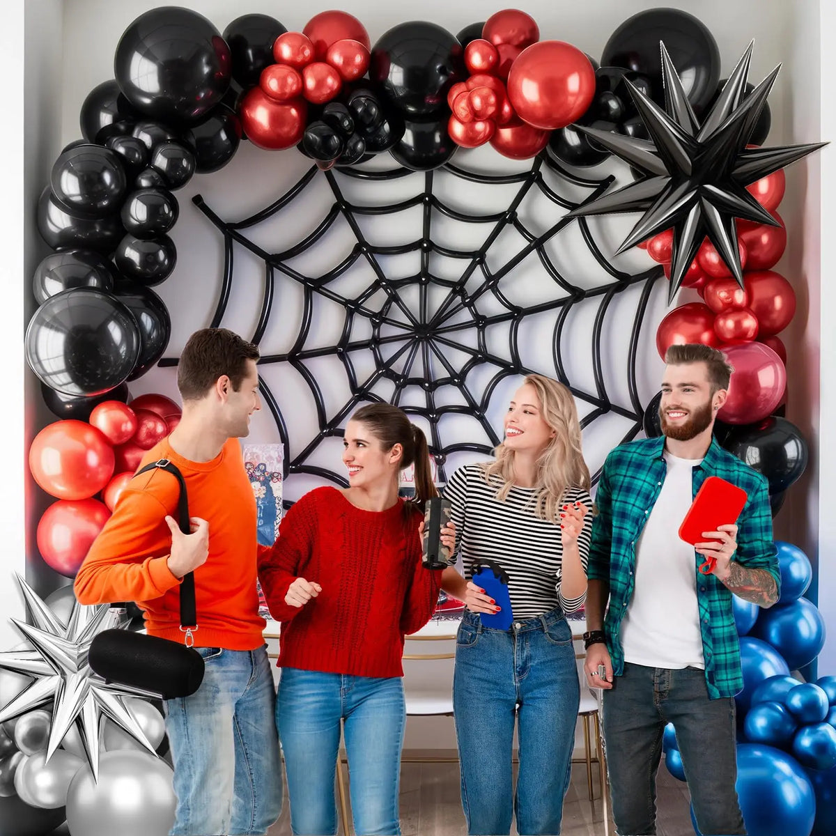 Four people posing in front of a balloon garland featuring blue, red, and black balloons.