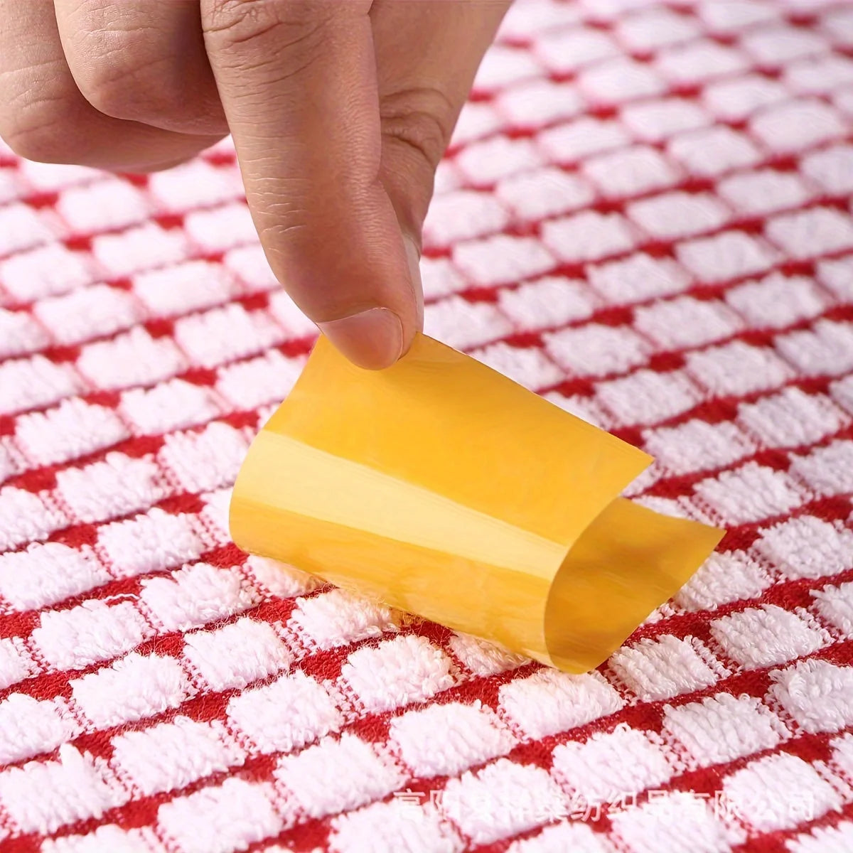 A hand is holding a yellow absorbent cotton cleaning cloth on a red checkered towel.
