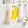 A yellow silicone kitchen scraper hanging on a white rack.