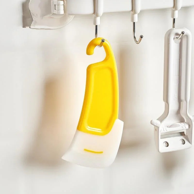 A yellow silicone kitchen scraper hanging on a white rack.