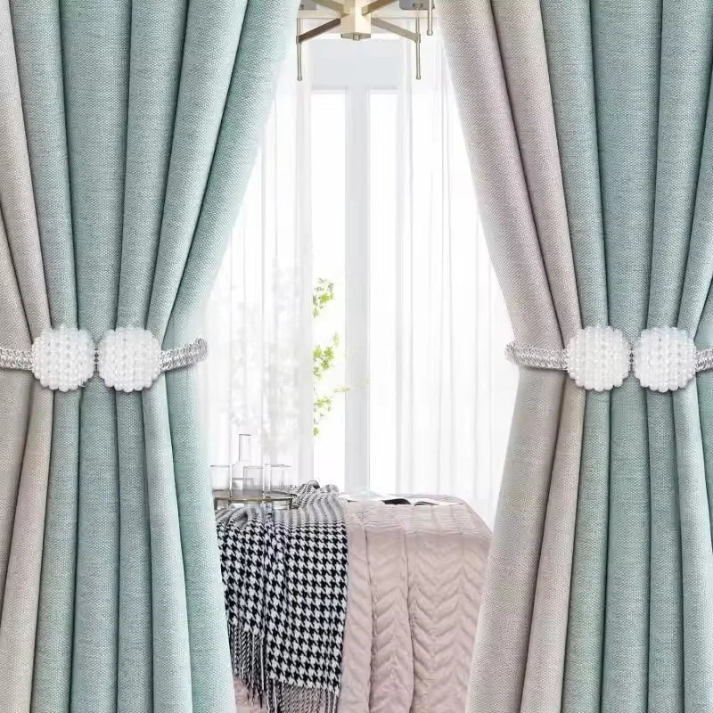 Un ensemble de tire-rideaux magnétiques en perles, vert clair et beige, encadrant une fenêtre.