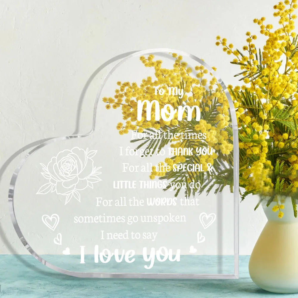 A clear acrylic heart-shaped keepsake engraved with 'I love you mom' and surrounded by yellow flowers.