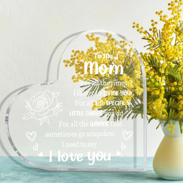 A clear acrylic heart-shaped keepsake engraved with 'I love you mom' and surrounded by yellow flowers.