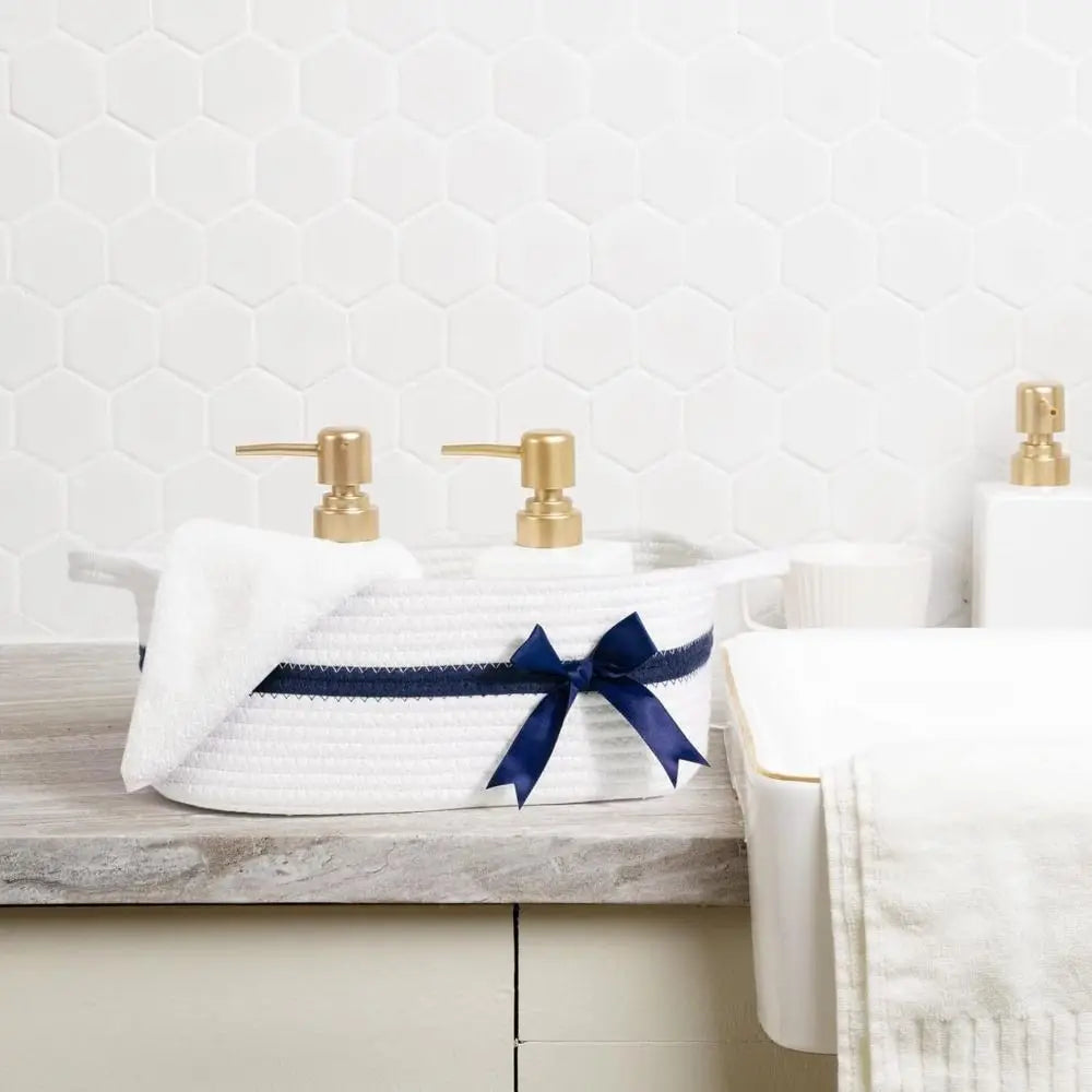 A woven cotton rope storage basket with a blue ribbon and brass faucets sits on a light gray countertop.