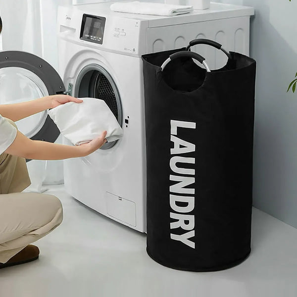 A black laundry basket with padded handles is placed next to a white washing machine.