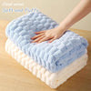 A hand is gently touching a fluffy blue cloud velvet bath towel layered on a thick white towel.