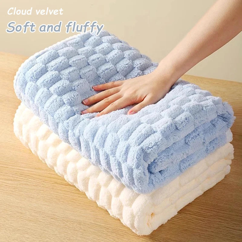 A hand is gently touching a fluffy blue cloud velvet bath towel layered on a thick white towel.