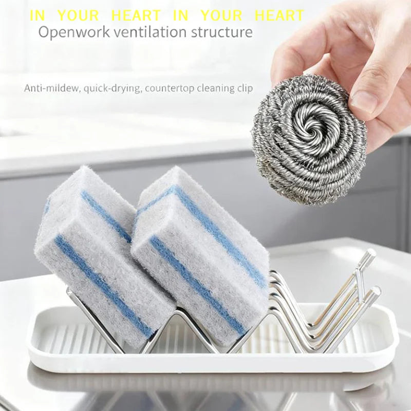 A hand holds a coiled gray cleaning sponge, with two blue-striped sponges resting in a stainless steel rack on a white tray.