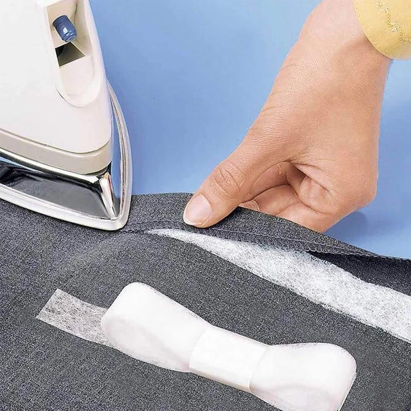 Una mano aplica cinta de dobladillo para forrar tela pesada de color gris oscuro para coser.