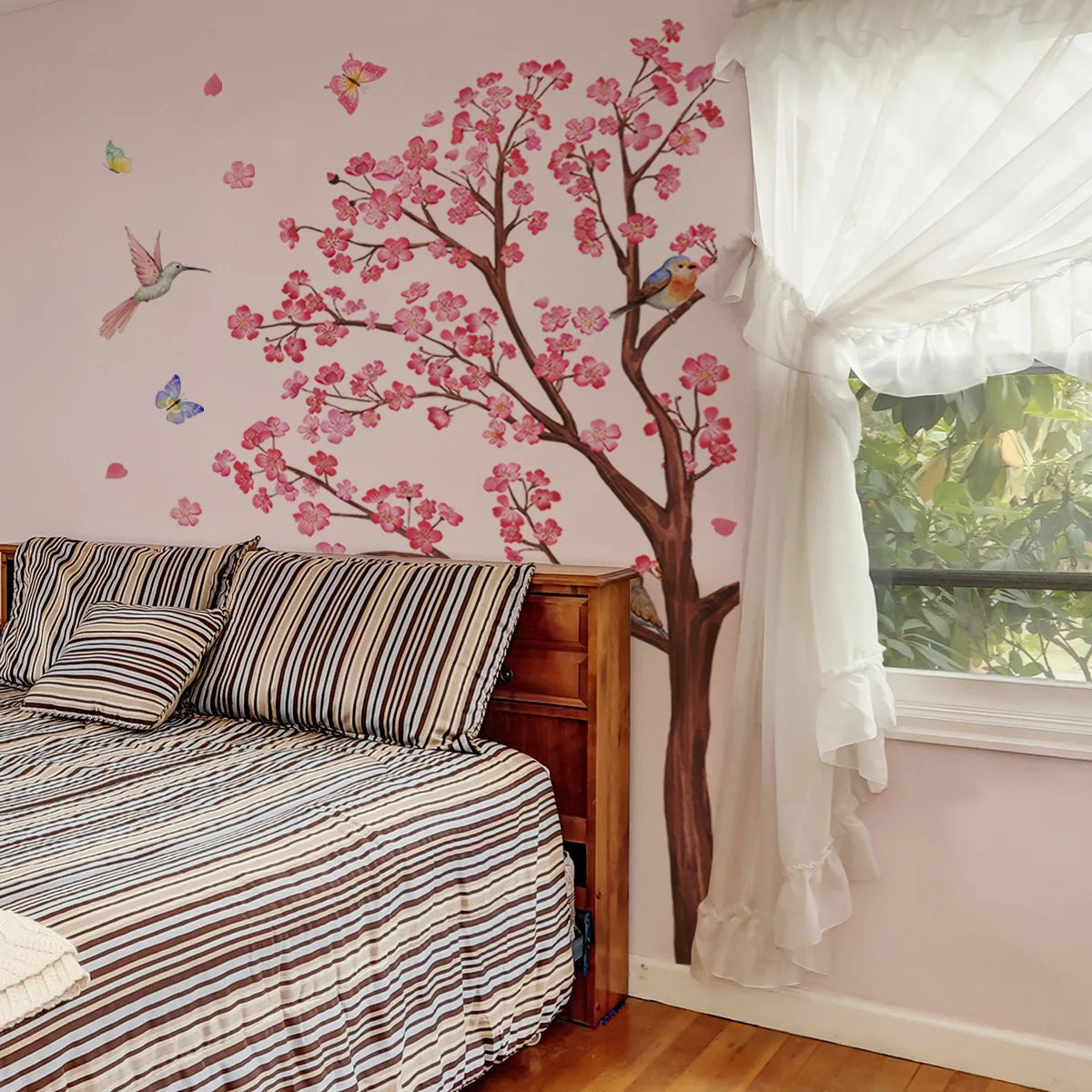 A bedroom featuring a pink floral wall mural of peach tree branches and a white sheer curtain.