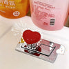 A heart-shaped toilet presser button is displayed on a silver tray next to a bottle of liquid air freshener.