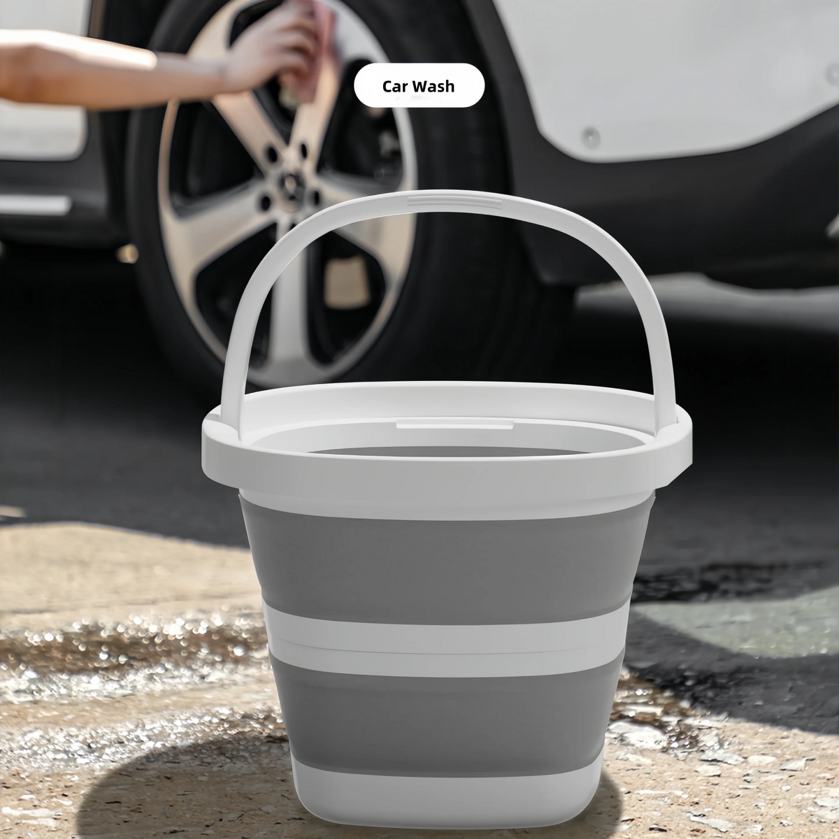 A white collapsible water bucket sitting on a concrete surface with a car in the background.