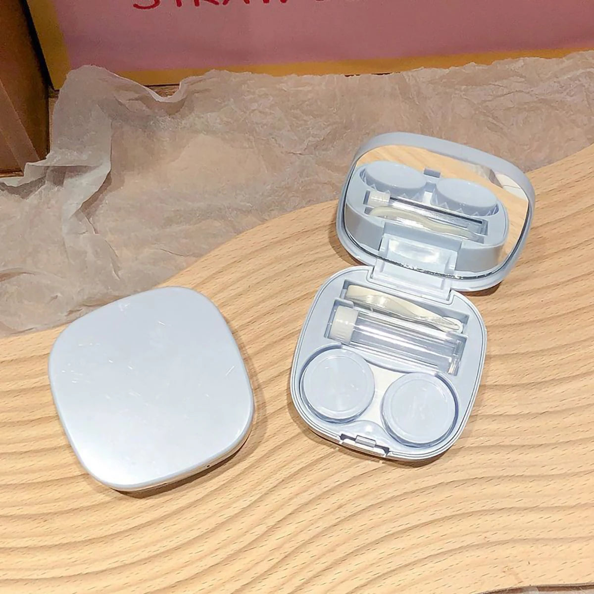 Offene, klare Kunststoffbox für Kontaktlinsen mit mehreren Fächern auf einer hellen Holzoberfläche.