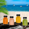 A set of leak-proof clear juice bottles filled with orange, pink, yellow, and green juices on a wooden surface near a beach b