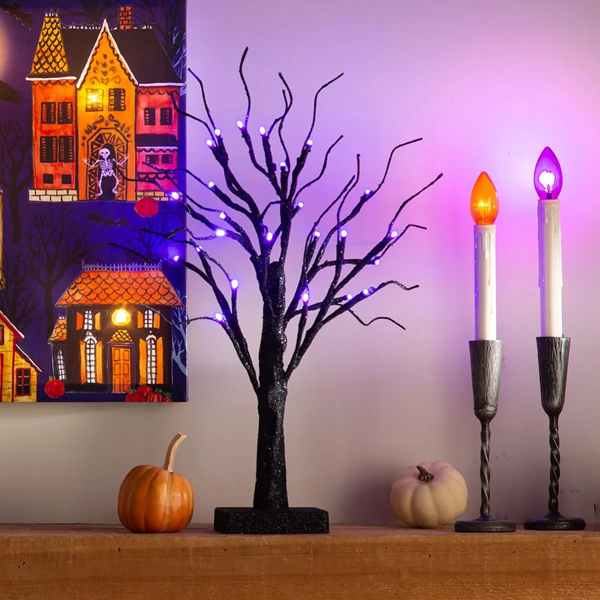 Dunkler Birkenbaum mit lila LED-Lichtern vor violetter Wand und zwei hohen Kerzen.