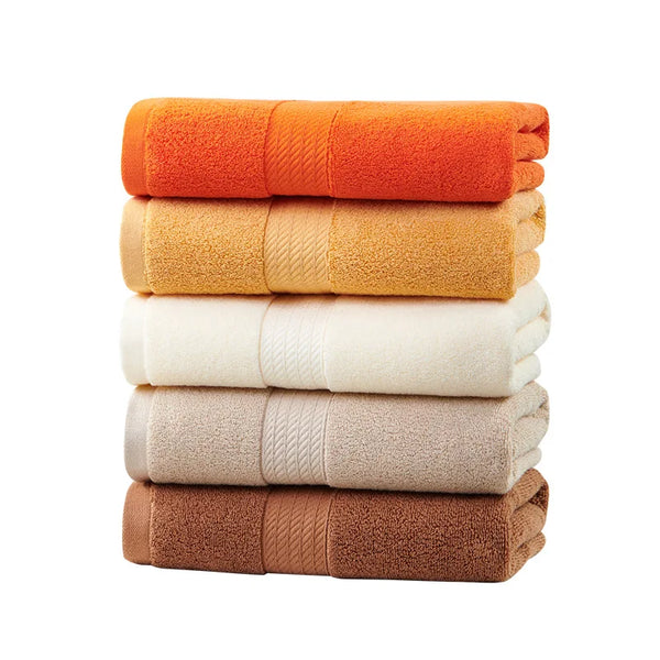 A stack of five folded face towels in shades of orange, beige, and brown.