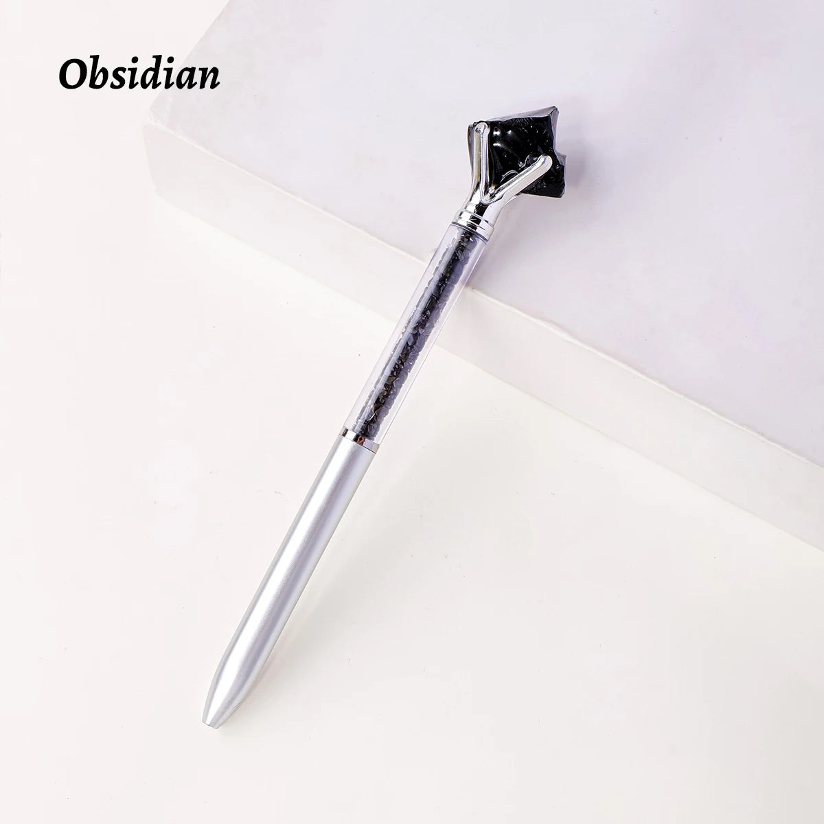 A silver crystal pen with a black, jagged tip resting on a white surface.
