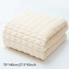 A stack of thick, cream-colored terry cloth bath towels folded neatly on a white surface.