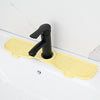A yellow silicone sink splash guard mat with a black faucet handle is placed on a white countertop.