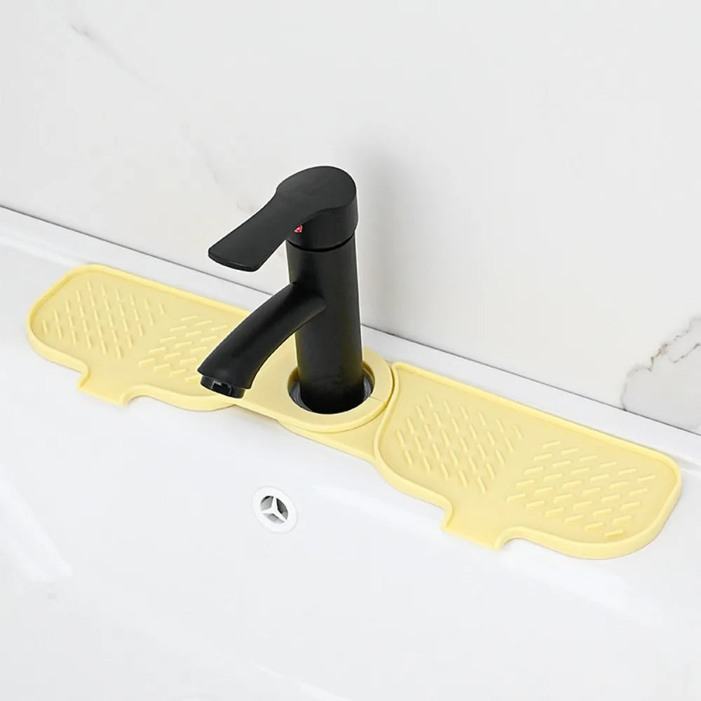 A yellow silicone sink splash guard mat with a black faucet handle is placed on a white countertop.