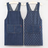 A pair of dark blue striped denim aprons hanging on a hanger.