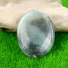 A smooth, oval gray quartz thumb stone resting on bright green grass.