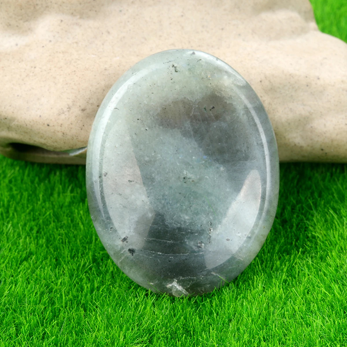 A smooth, oval gray quartz thumb stone resting on bright green grass.