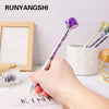 A hand holds a silver pen with a purple amethyst crystal tip resting on a white surface.