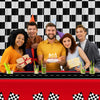 A family of four celebrating with birthday candles in front of a black and white checkered foil curtain backdrop.