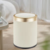 A cylindrical trash can with a gold rim and white ribbed body sits on a wooden surface.