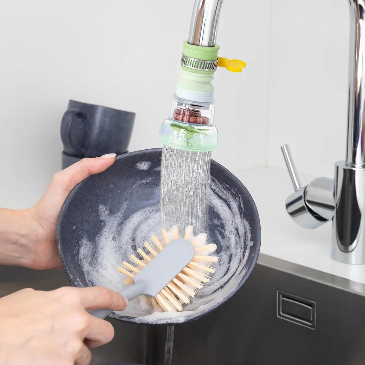 Hände benutzen einen rotierenden Küchenarm, um einen Teller zu reinigen.