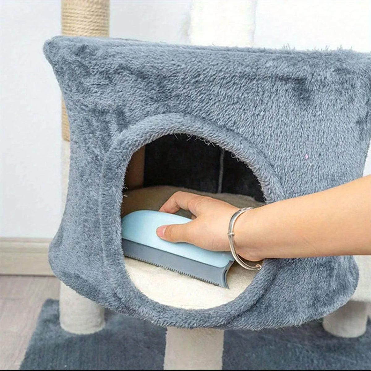 A hand is using a pet hair remover brush on the opening of a gray, textured pet toy.
