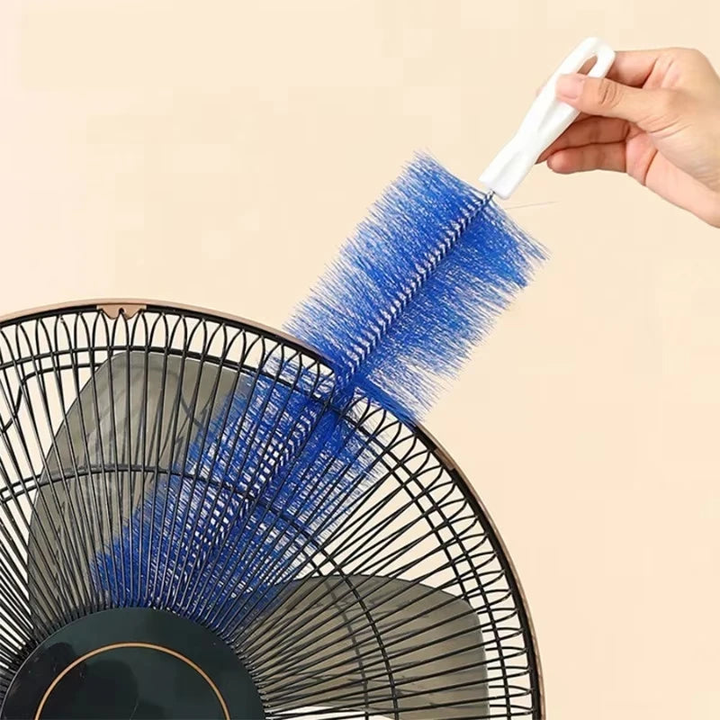 A hand holds a blue cleaning brush with a white handle, positioned against a black fan grille.