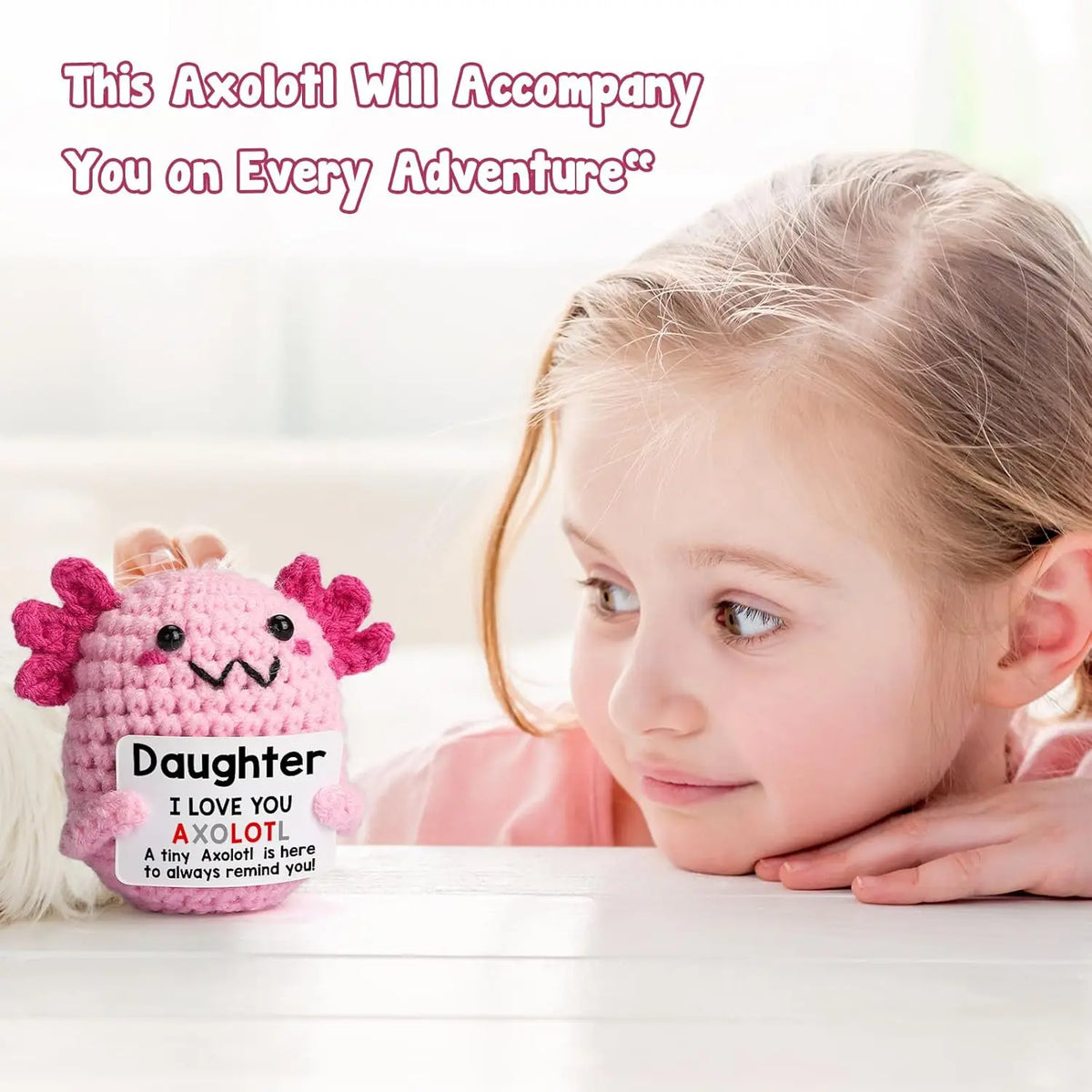 A young girl smiles while holding a pink crocheted axolotl figurine.