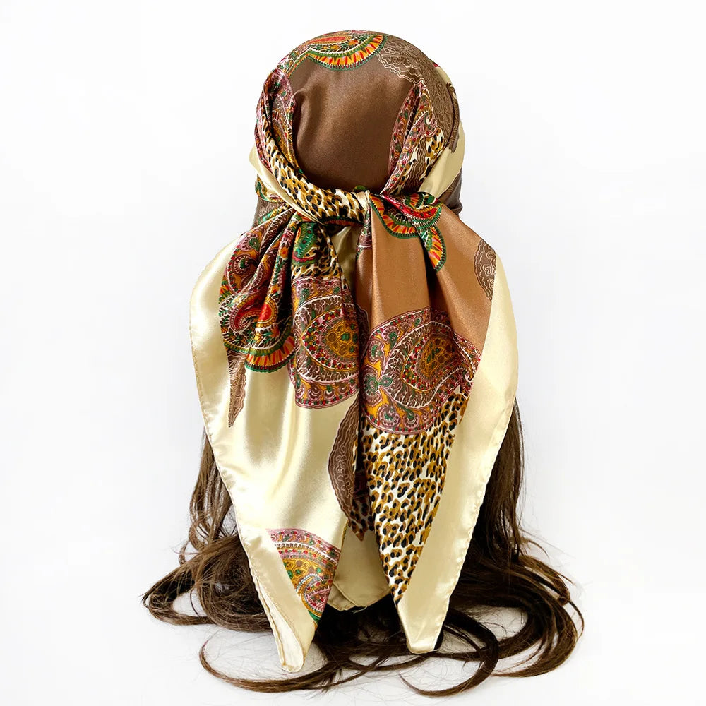 A women's square paisley print scarf in gold and brown tones tied around a dark brown ponytail.
