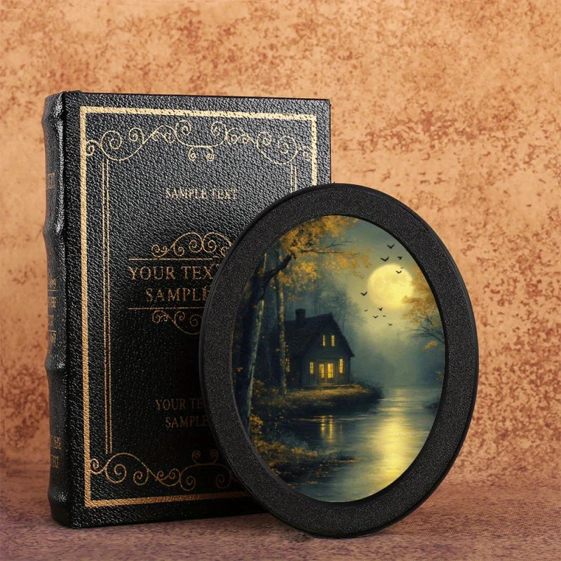 A black leather-bound sample text book and a round photo frame with a moonlit landscape.