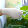 A hand wearing a light beige disposable nitrile glove gently touches a green leaf.