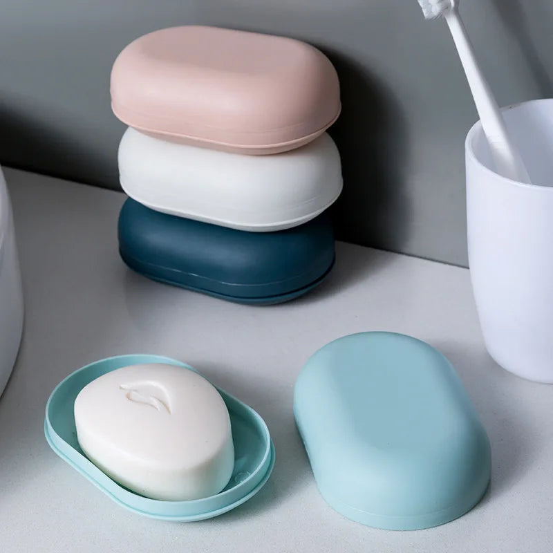A stack of three pink, white, and blue portable soap holders with lids, alongside a single light blue holder.
