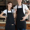 Two models wearing black all-purpose canvas aprons in a kitchen setting.
