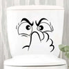 White toilet lid featuring a black cartoon face with wide eyes and a raised hand.