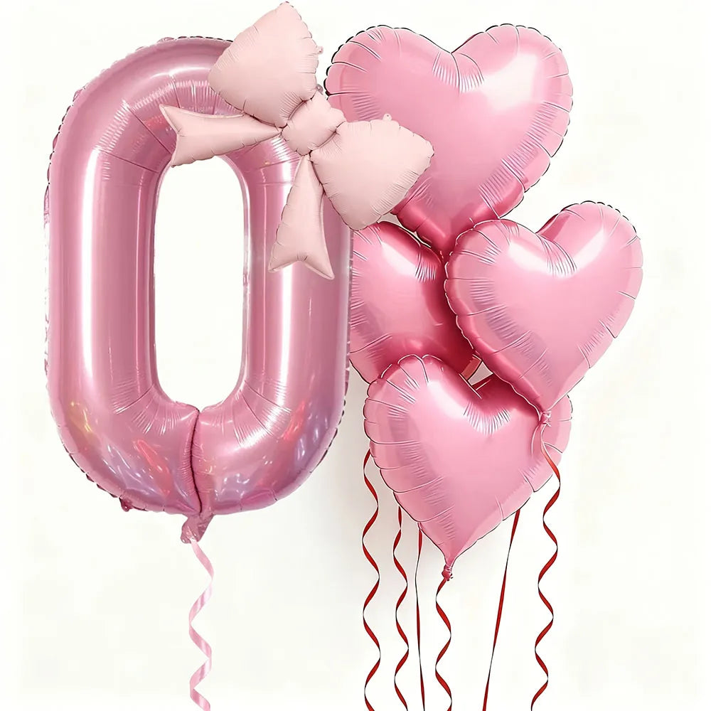 Un set de seis globos de látex en forma de corazón rosa, incluyendo el número cero, atados con cintas rosas.