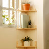 A boho triangle floating wall shelf displaying potted greenery and books against a light wall.